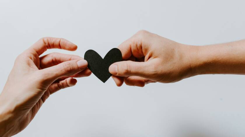 Kaksi kättä pitelee yhdessä pientä askarreltua sydäntä. Kuvaaja: Kelly Sikkema / Unsplash.